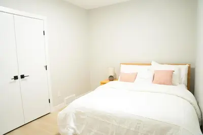 a white bedroom with a white bed with pink pillows at The Old Trafford - Stylish 2 bed suite in Calgary