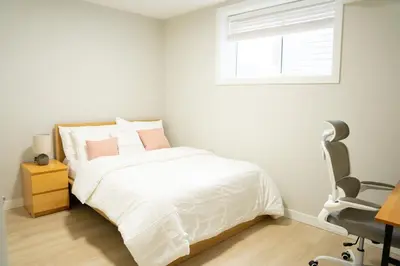 a bedroom with a bed and a chair and a window at The Old Trafford - Stylish 2 bed suite in Calgary