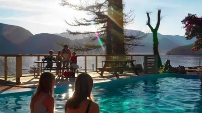a group of people sitting around a swimming pool next to the water at Ozarks Luxurious Lakeside Villa at Harrison Lake in Harrison Hot Springs