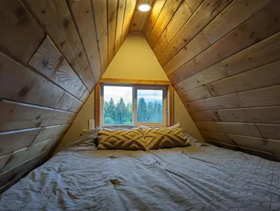 a bed in a room with a large window at Tree Ring Cabin on 33 Acre Farm in Powell River