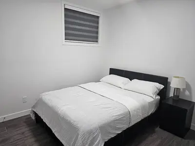 a white bedroom with a large bed with a window at New 2 bdrm basement suite Seton in Calgary