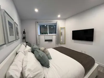 a white bedroom with a large bed and a flat screen tv at Serenity 1BR & 1 DEN Home at Folsom Ave in Coquitlam