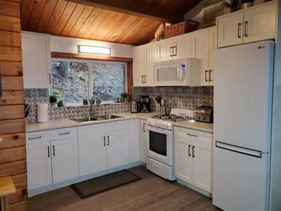 a kitchen with white cabinets and a white refrigerator at West facing Waterfront Cottage with private beach & buoy & dock access in Blind Bay