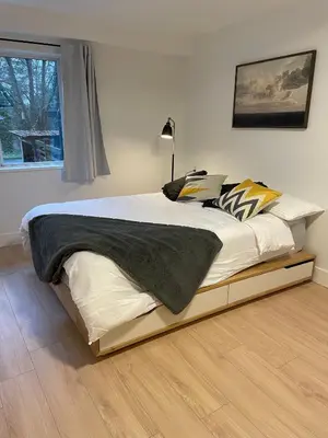 a bedroom with a large bed with a wooden floor at Spacious Forested Garden Suite in North Vancouver