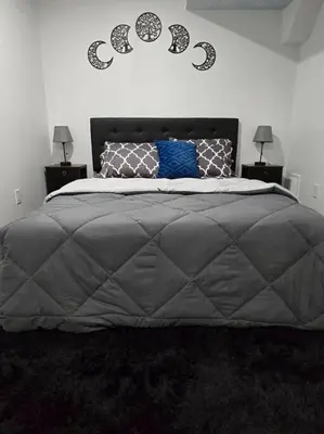 a bedroom with a large gray bed with two lamps at Cozy New 1 bed basement suite in Edmonton