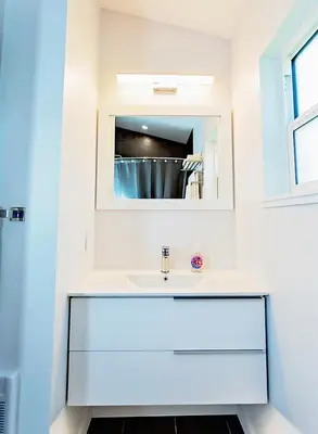 a white bathroom with a sink and a mirror at LuxQuarters Bumbleberry Guest House in Kitimat