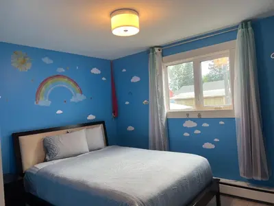 a bedroom with a bed with a rainbow and clouds at Little Holiday Home in Yellowknife