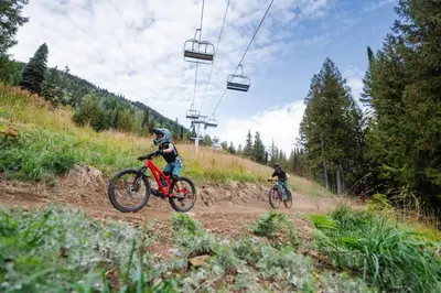 two people riding bikes on a dirt road with a ski lift at White Wolf in Rossland