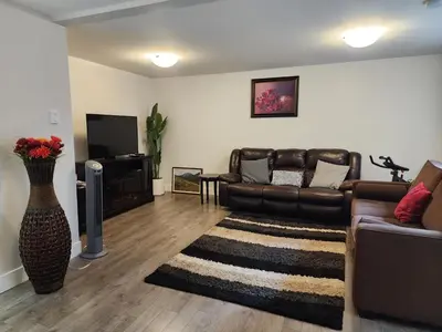 a living room with a leather couch and a television at Cozy Royal Bay Suite in Victoria