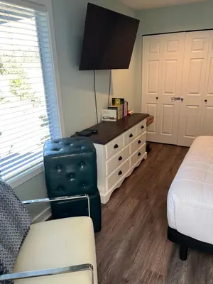 a living room with a bed and a dresser with a tv at Aloha Cottage, Nanoose Bay - 2 Bdrm Oceanfront Unit with Private Deck in Nanoose Bay