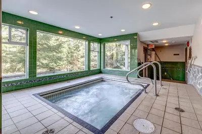 a hot tub in a room with green walls and windows at Greystone Lodge 214 Ski-in Out in Whistler