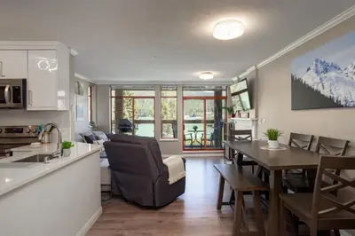 a kitchen and living room with a table and a couch at 2BR in Nicklaus North Clubhouse, Lake and Mountain Views, Gas Fireplace, Parking in Whistler