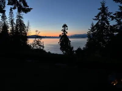 a sunset over a body of water with trees at Tyee Beach Oasis Bed and Breakfast in Nanoose Bay
