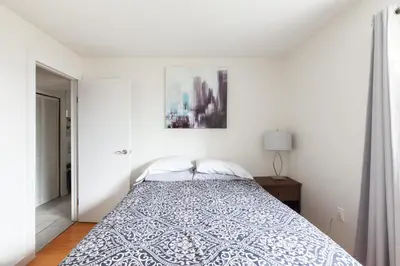 a white bedroom with a bed and a picture on the wall at PNE Delight in Vancouver
