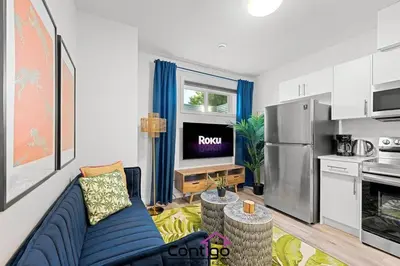 a living room with a blue couch and a kitchen at The Den, Centrally Located Suite, King Bed, WiFi! in Edmonton