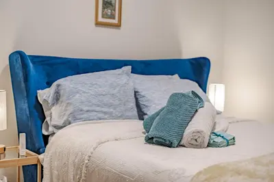 a bed with a blue head board with towels on it at Luxe Suite close to Spruce Meadows in Priddis