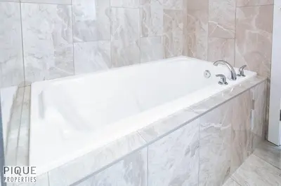 a white bath tub in a bathroom with marble tiles at Modern Retreat - 3 King Beds - Garage - WiFi - Sleeps 10 in Edmonton