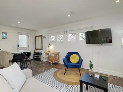 a living room with a blue chair and a television at Fairfield Estate Coach House - 30-Day Stay, steps from Cook Street Village by Victoria Prime! in Victoria