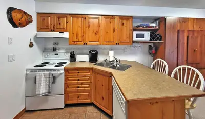 a kitchen with wooden cabinets and a stove and a sink at Timberline Village #12 home in Sun Peaks