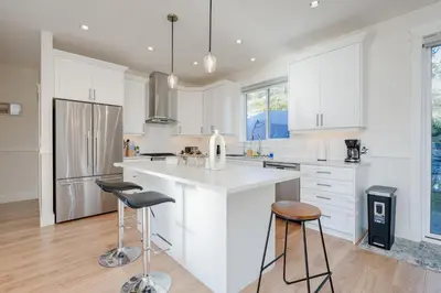 a kitchen with white cabinets and a counter and stools at Elegant Home In Victoria,BC in Langford