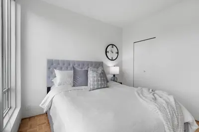 a white bedroom with a bed with a clock on the wall at Central Downtown Highrise Condo in Vancouver
