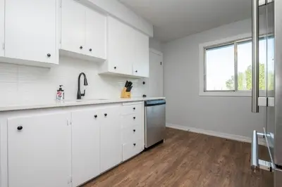 a white kitchen with white cabinets and a window at Highland Park Upper Suite in Calgary