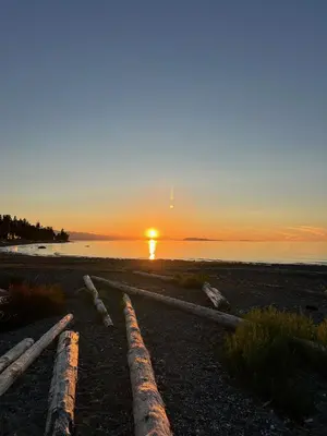 a sunset over the ocean with logs on a beach at Five Gables B&B in Qualicum Beach