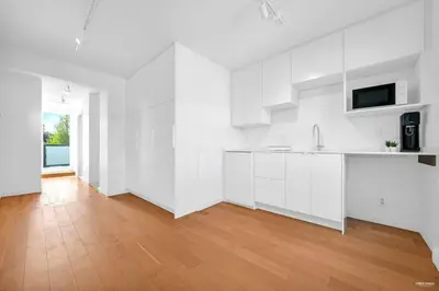 a white kitchen with white cabinets and a wooden floor at Charming East Van Home Near DT and Commercial St in Vancouver