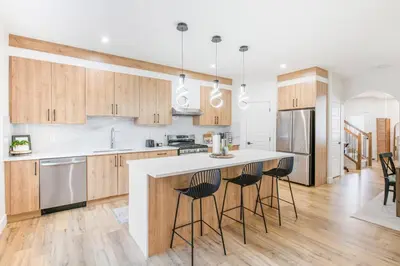 a kitchen with wooden cabinets and a island with bar stools at Luxury Family Home - Sleeps 10 - King Bed in Nisku