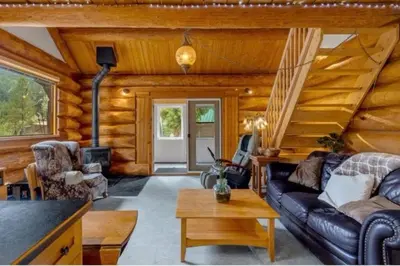 a log cabin living room with a couch and a staircase at Authentic lofted log cabin with hot tub in Kelowna