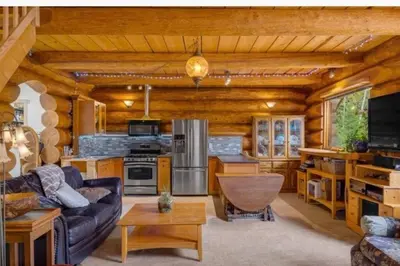 a living room with a couch and a kitchen at Authentic lofted log cabin with hot tub in Kelowna