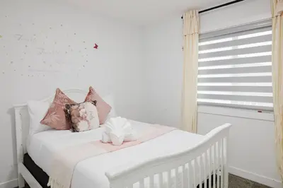 a white crib in a white room with pink pillows at Executive Modern Family Haven for Short Stays in Edmonton