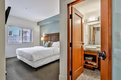 a bedroom with a bed and a bathroom with a sink at Woodland Retreat 2 Bedroom in Canmore