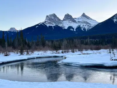 a river in the snow with mountains in the background at Chic Urban Sanctuary in the Heart of Down in Canmore