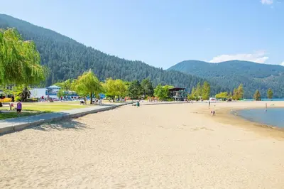 a beach with people on it with mountains in the background at Echo Beach, 2 Bed, Lake View and Walkable to Beach in Harrison Hot Springs