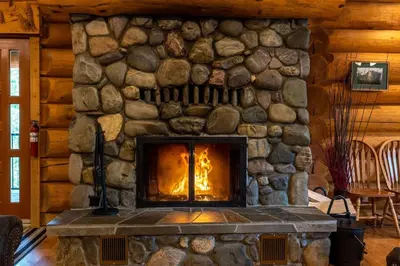 a stone fireplace in a log cabin with a fire at Alders Chalet by Fernie Central Reservations in Fernie