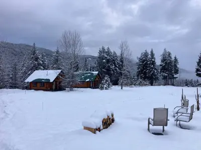a snow covered field with a cabin in the background at Log lofted rustic cabin in woods in Kelowna