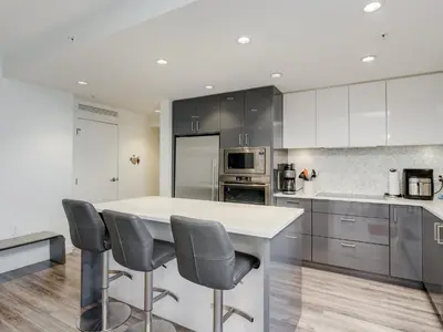 a kitchen with a white counter and chairs in it at Escher Escape - Art-filled retreat with work desk by Victoria Prime! in Victoria