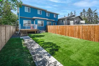 a backyard with a blue house and a wooden fence at Near Downtown, Large 3BR! FREE Banff Pass, Netflix, Parking! in Calgary