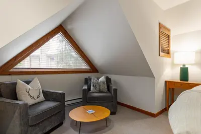 a attic bedroom with two chairs and a bed and a window at 2BR in Gleneagle, Heated Flooring, Wood Burning Fireplace, Shuttle to Gondola in Whistler