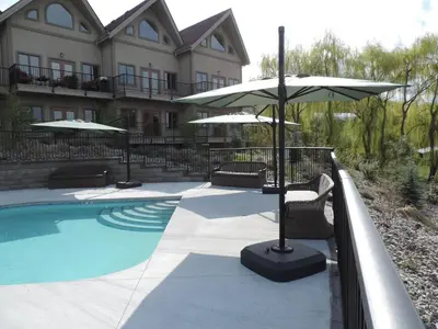 a pool with two umbrellas and chairs next to a building at The Castle at Swan Lake in Vernon