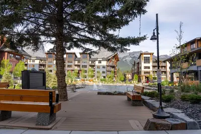 a park with a tree and benches and buildings at Modern Mountain Oasis Top floor 2 level 2bd in Canmore