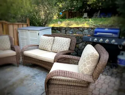 two wicker chairs and a table in front of a stone wall at Westshore Garden Escape in Victoria