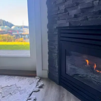 a fireplace with a fire in it next to a window at High Tide - Waterfront bachelor in Tofino