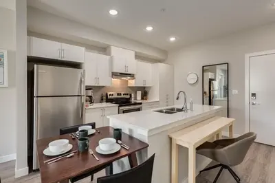 a kitchen with white cabinets and a wooden table with chairs at Free Underground Parking, Pet Friendly Apartment in Calgary