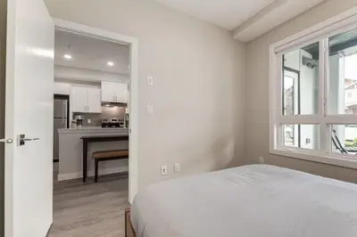 a white bedroom with a bed and a kitchen at Free Heated Parking, Quick DT Access in Calgary