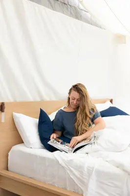 a woman sitting on a bed reading a book at Lux Remote Glamping Hideaway in Ucluelet