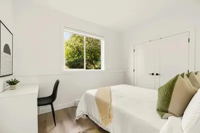 a white bedroom with a bed and a desk and a window at Cozy Saanich Cottage ideal location to UVIC and Downtown in Victoria