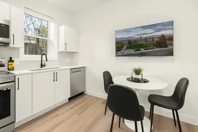 a kitchen with white cabinets and a white table and chairs at Cozy Saanich Cottage ideal location to UVIC and Downtown in Victoria