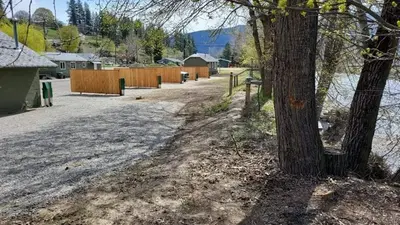 a fence and a tree next to a street at Riverside Court RV and Cabins in Grand Forks